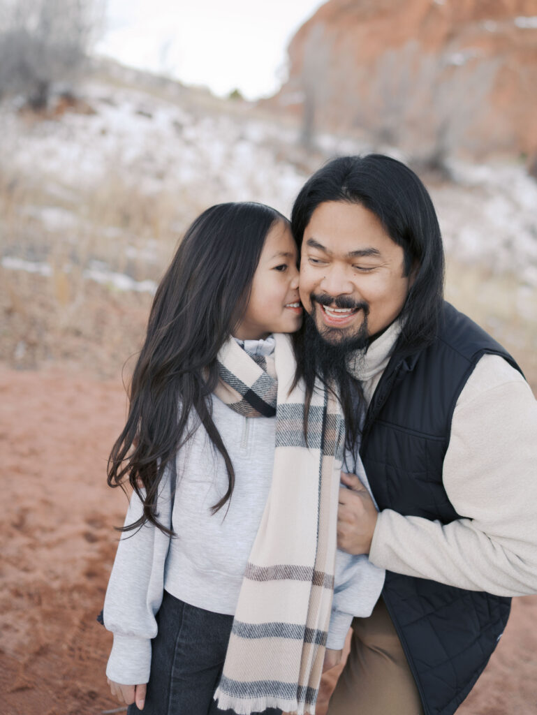 girl kissing dads cheek at red rock open space in colorado springs during family photo session with lauren bounds photography