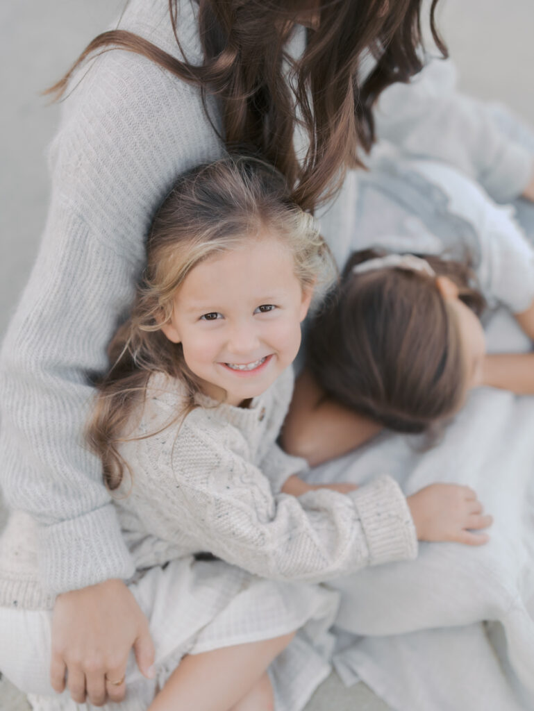 girl looking up at camera snuggled with mom and sister in colorado springs