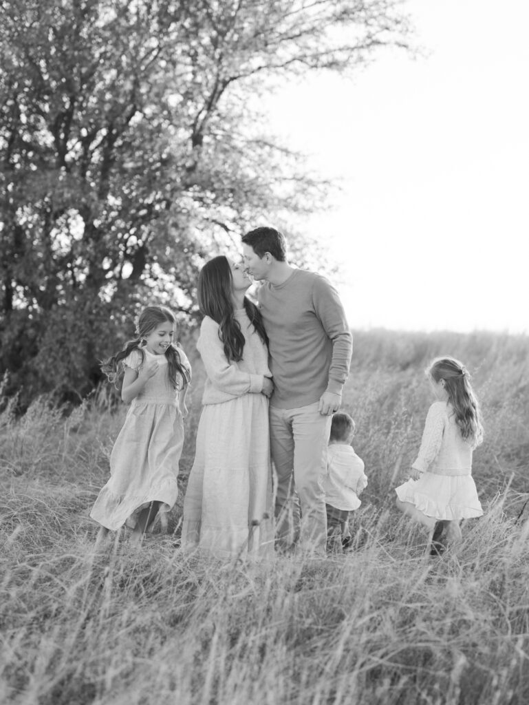 couple kisses while three kids run around them taken at a Colorado Springs family session by Lauren Bounds Photography