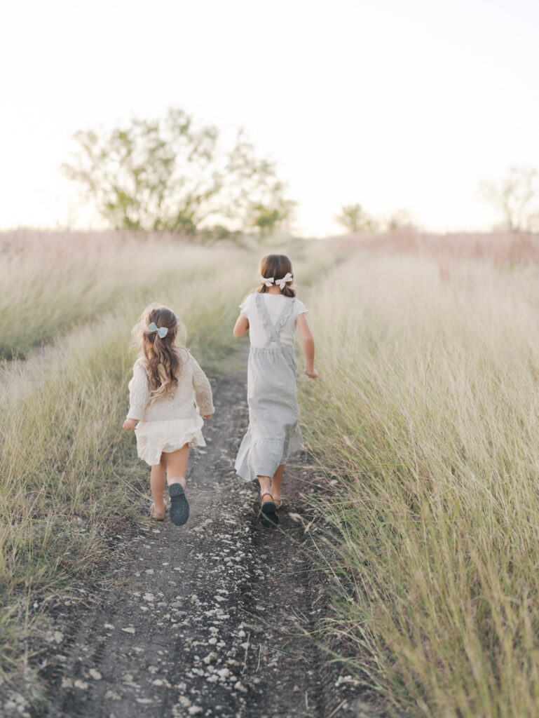 back view of two sisters running on a path in field, you can see the curls in their hair bouncing taken at a Colorado Springs family session by Lauren Bounds Photography