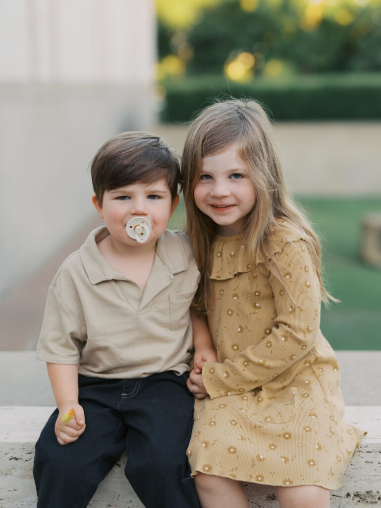 siblings sitting and looking at camera, little brother with pacifier in mouth in colorado springs