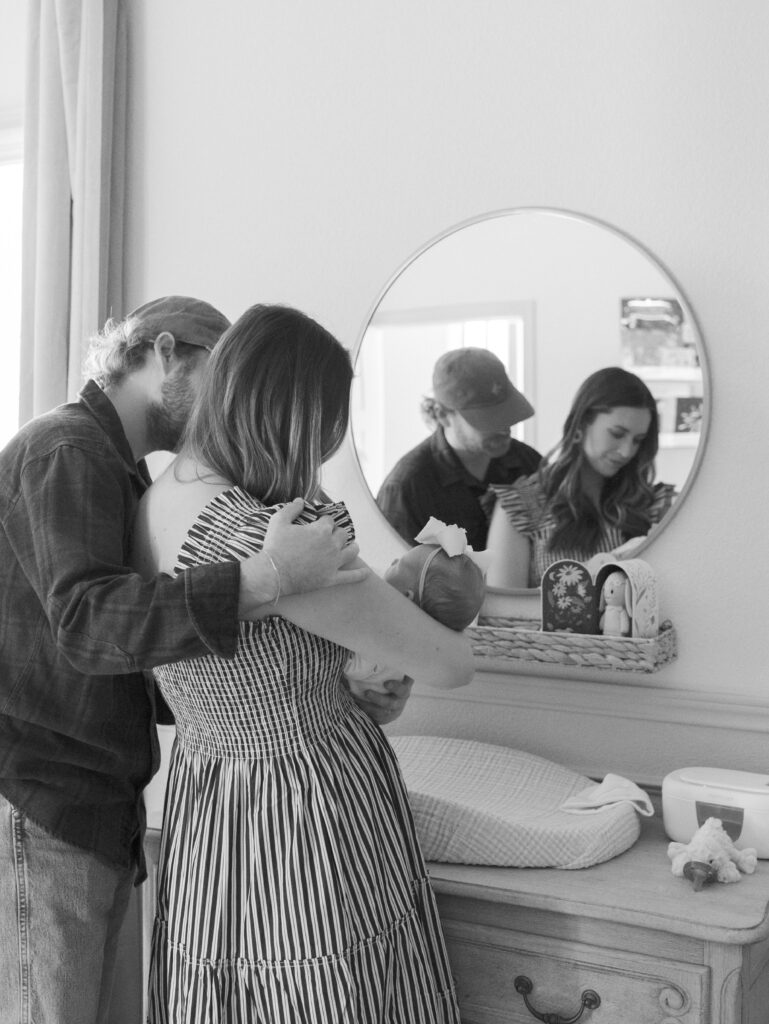 parents in nursery in front of mirror with newborn baby