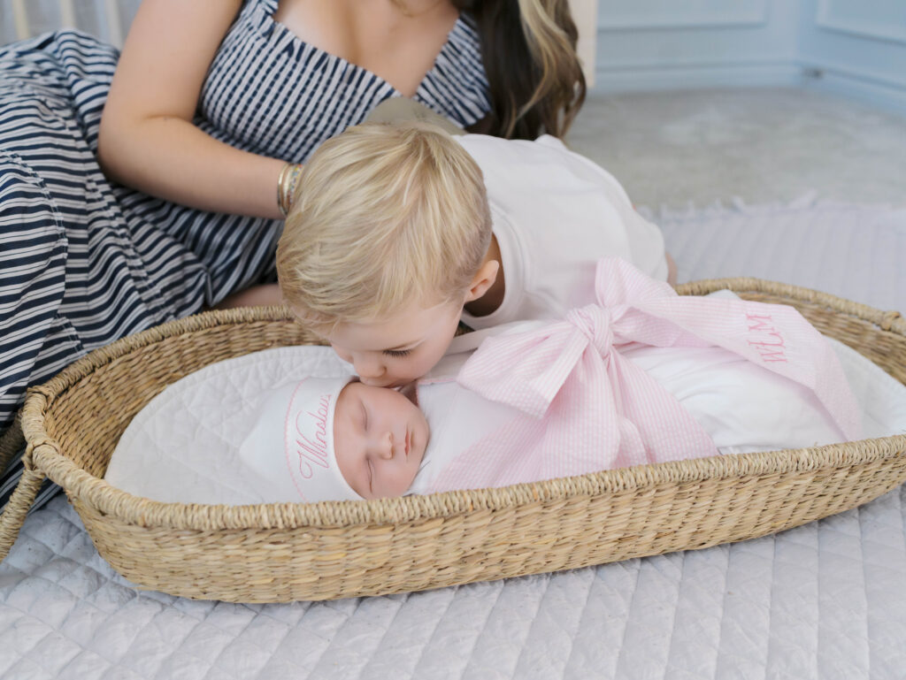 big brother leaning over to kiss newborn sister in basket Newborn Photos Colorado Springs