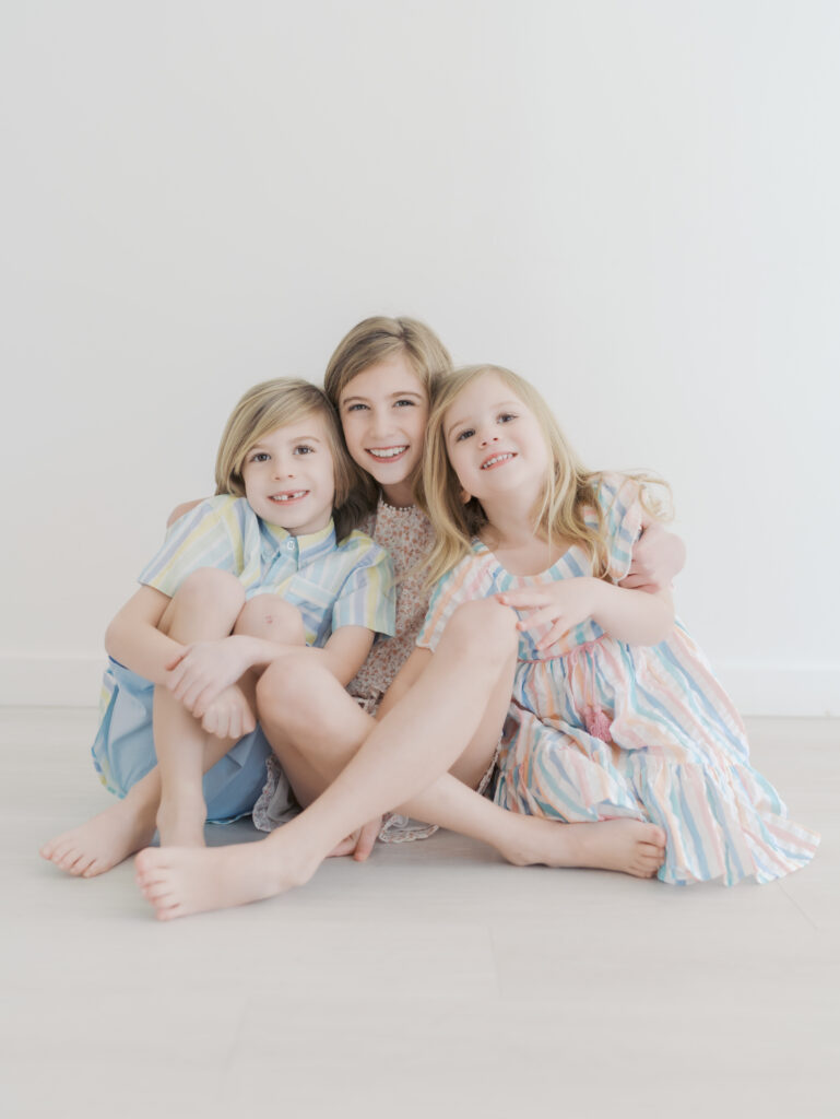 two sisters and one brother sit and snuggle close for sibling mini sessions colorado springs