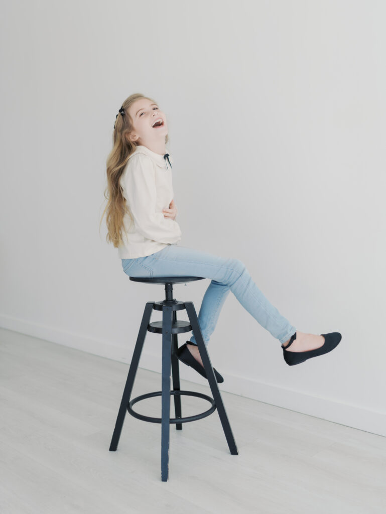 girl laughing while sitting on stool with one leg out