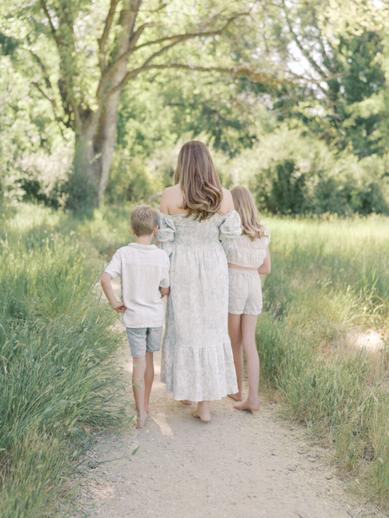 mom and two kids walking side by side on dirt pathway through trees