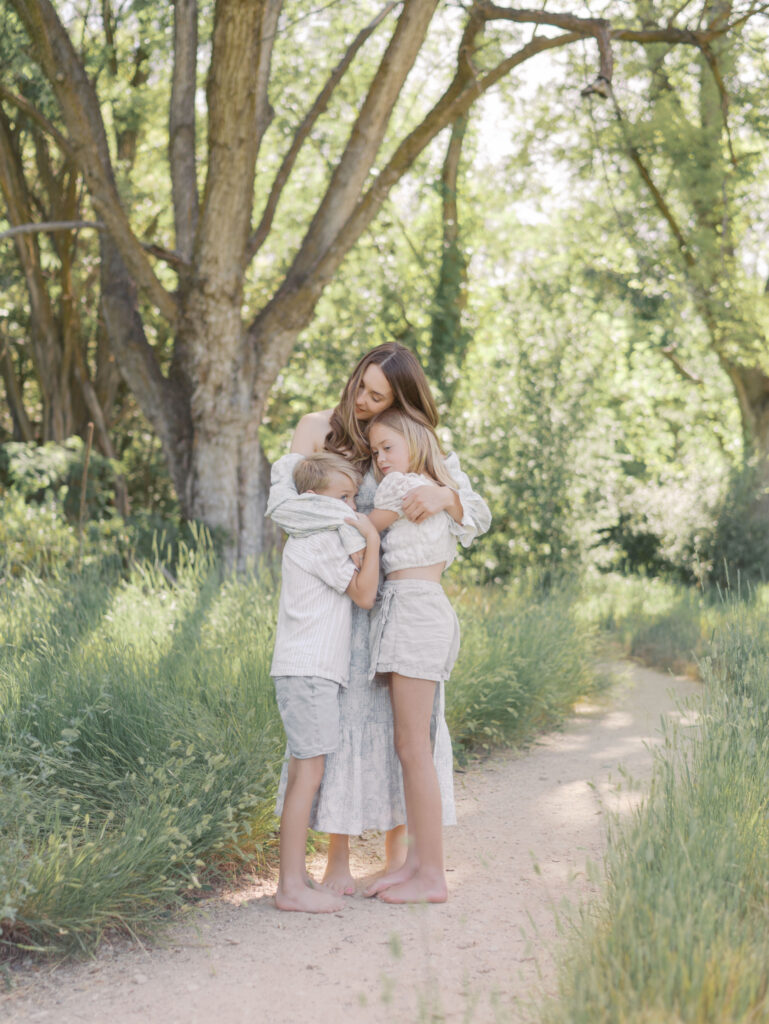 mom standing with kids hugging on walking path by trees