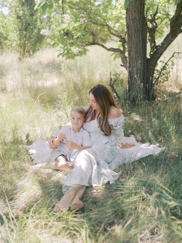 mom sitting with son on blanket in the grass looking down at him during spring family photography colorado