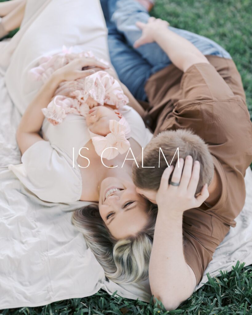 couple laying on blanket in grass.  dad propped up on arm smiling down at mom with baby on chest telling the Newborn Photography Experience Colorado Springs