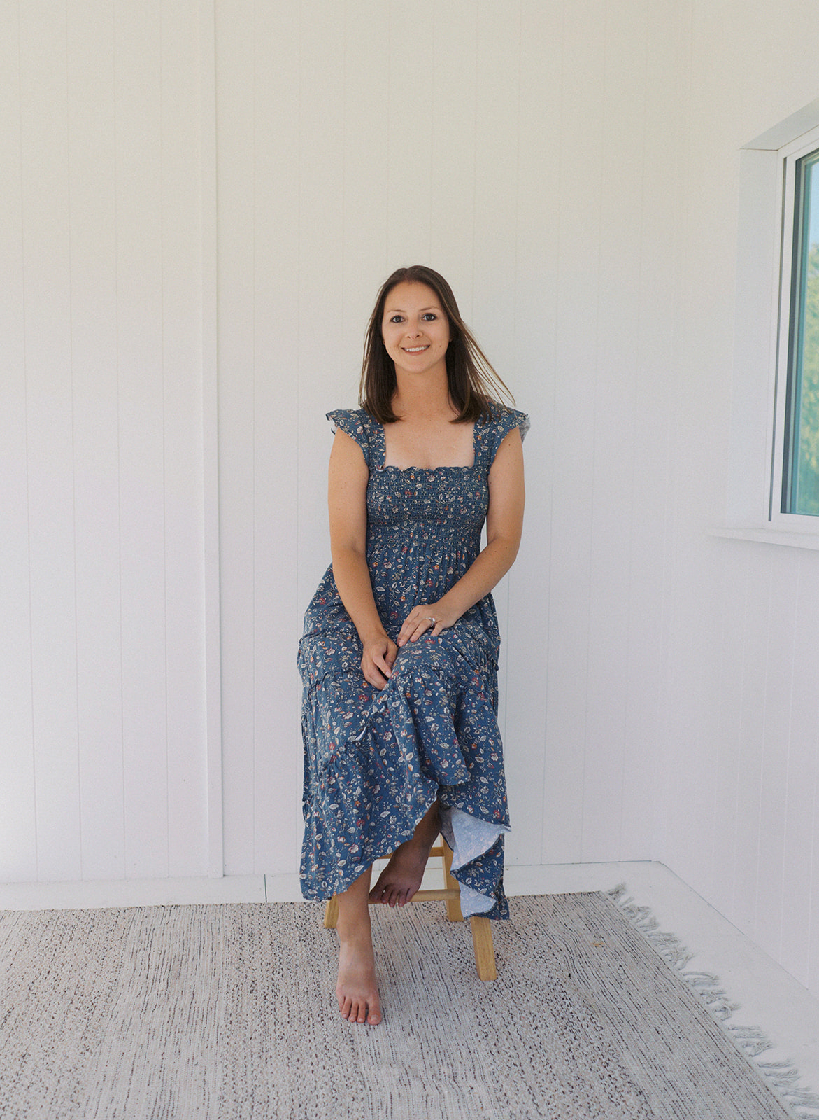 Lauren sitting on a still in a plain studio in blue floral dress, owner of lauren bounds photography, colorado springs photographer