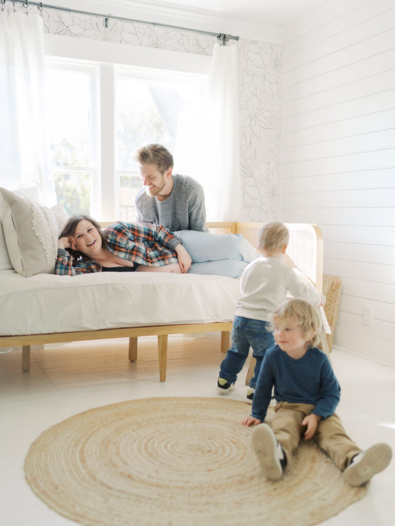 family at home playing while mom and dad lay on daybed for Maternity Photography Colorado Springs