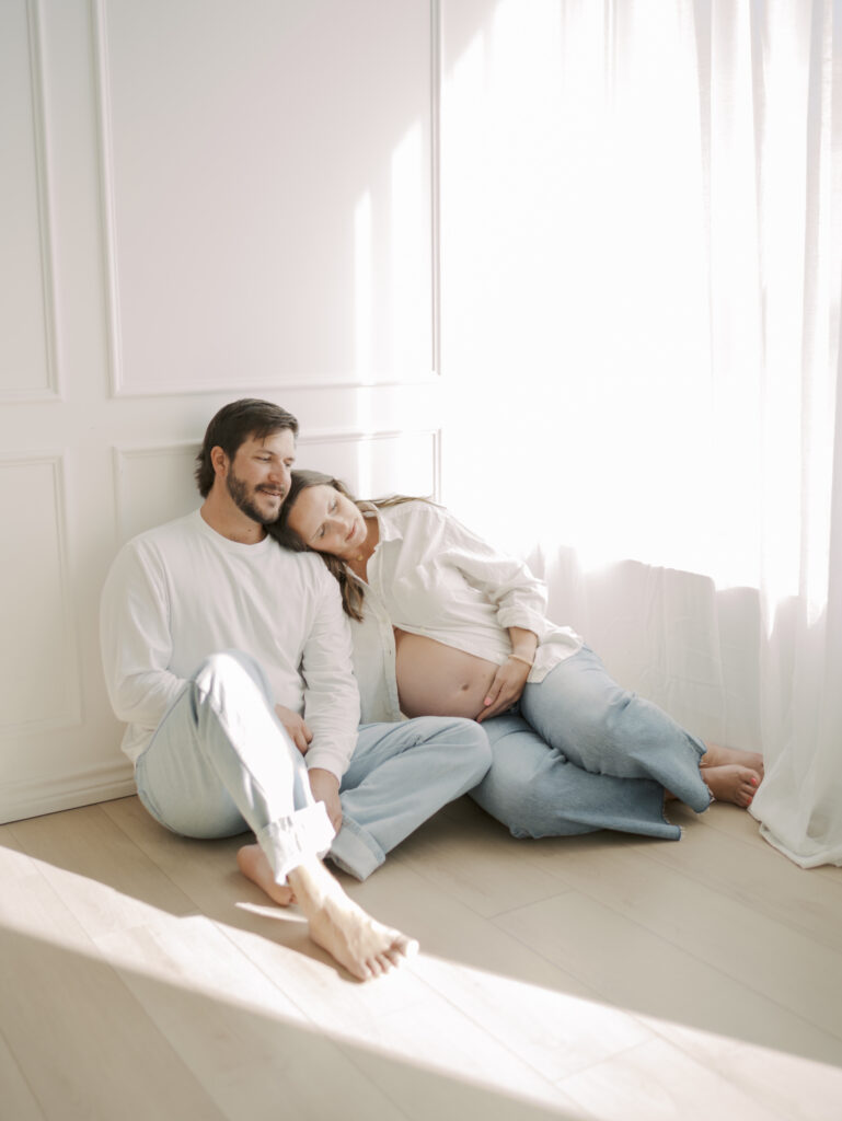 studio maternity photos in colorado springs showing expecting couple sitting on floor with wifes head on husbands shoulder