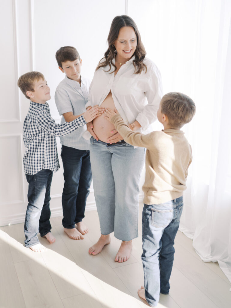 expecting mom and dad laying on couch kids around mom with their hands on her belly