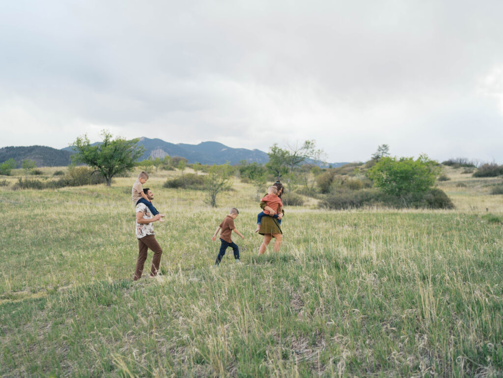 family of five walking with mountain in the background one kid on shoulders while one walks in the middle and the third is held by mom, taken by colorado springs colorado photographers Lauren Bounds 
