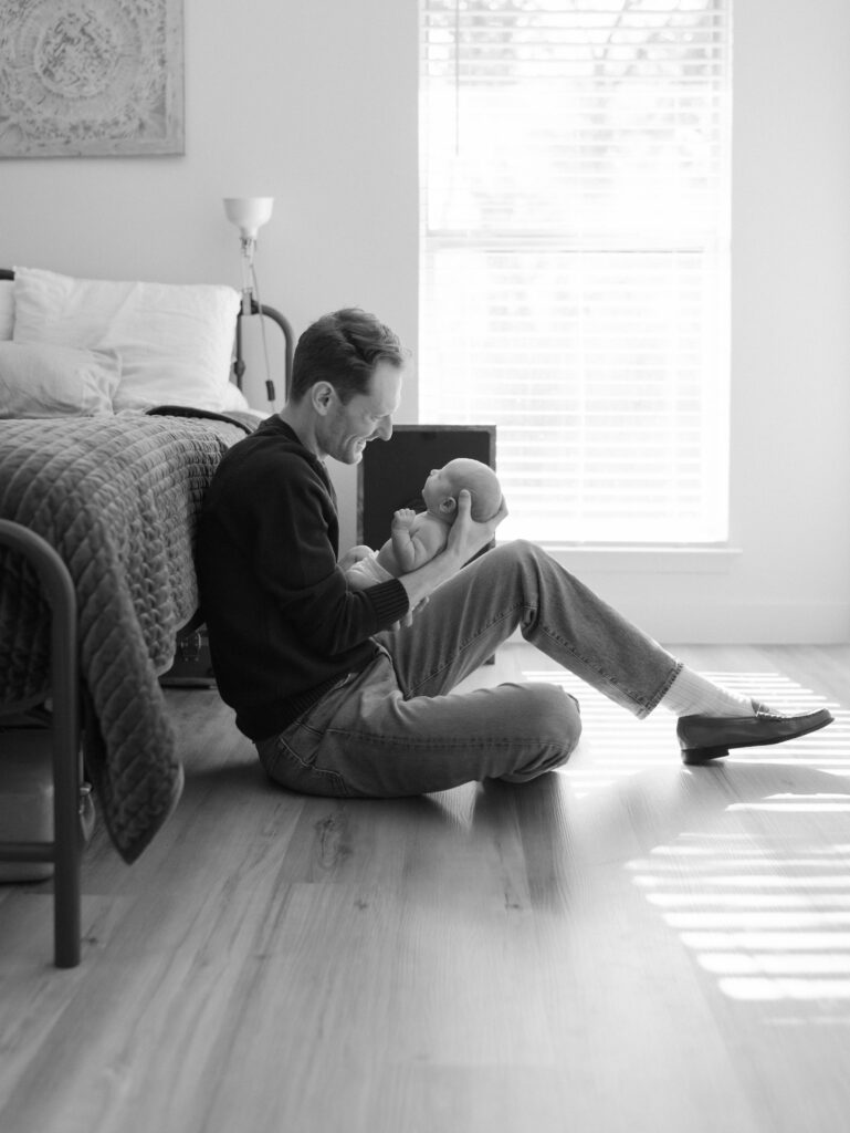 dad with newborn in hands sitting on floor for Colorado Springs Newborn Photography