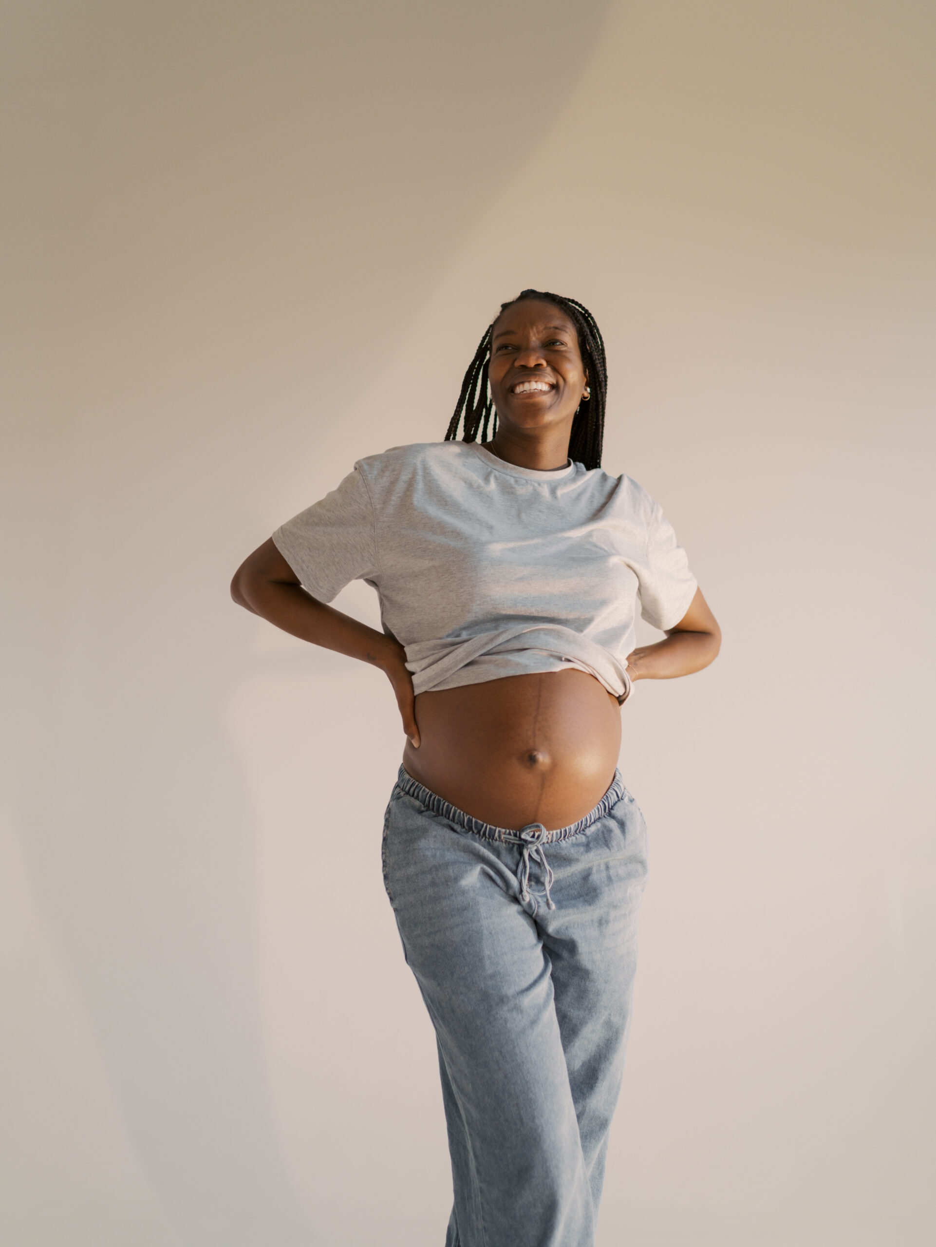 maternity photo of mom in studio in denver, co with hands in back and exposed belly smiling
