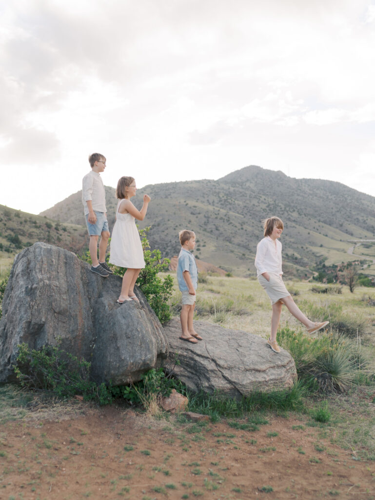 Four kids on big rocks walking for family maternity photos denver