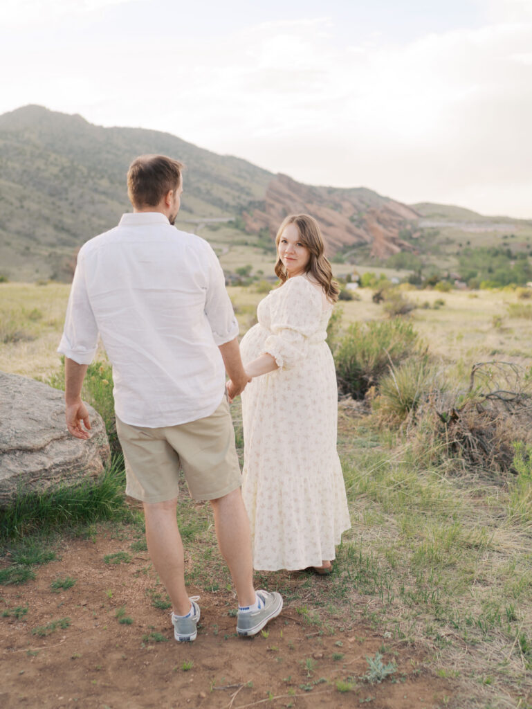 Expecting couple walking hand in hand with mom looking back at camera for family maternity photos denver