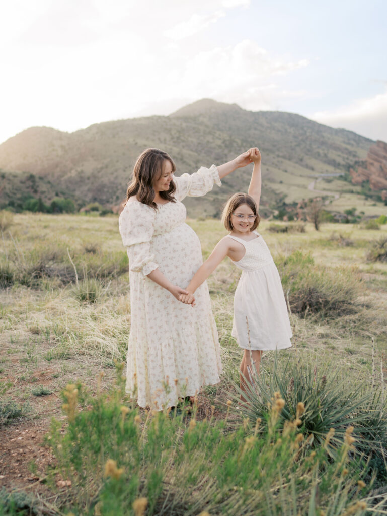 Expecting mom hand in hand with daughter with mountain in the background in Colorado