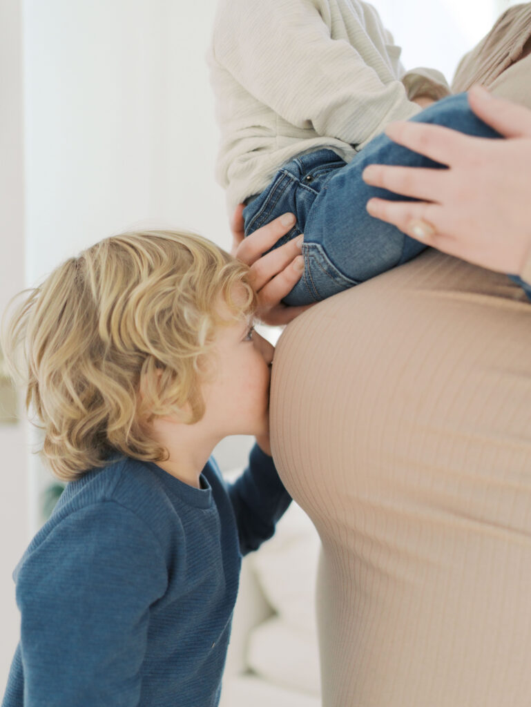 boy kissing pregnant moms belly while little brother sits on top of it