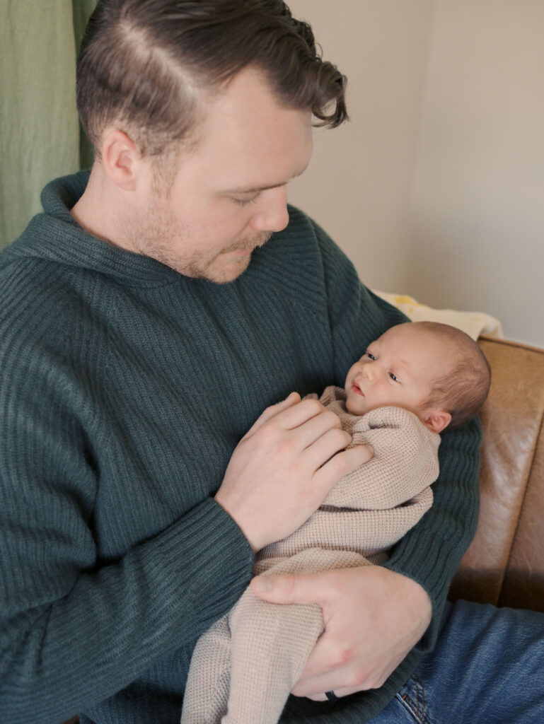 dad with newborn baby in arms sitting on couch for What to Expect During a Newborn Session | Colorado Springs Newborn Photographer